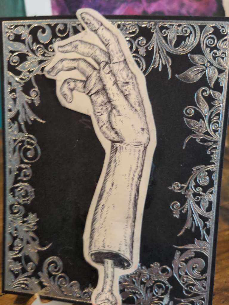 A disembodied hand with protruding bone against an ornate black and silver background